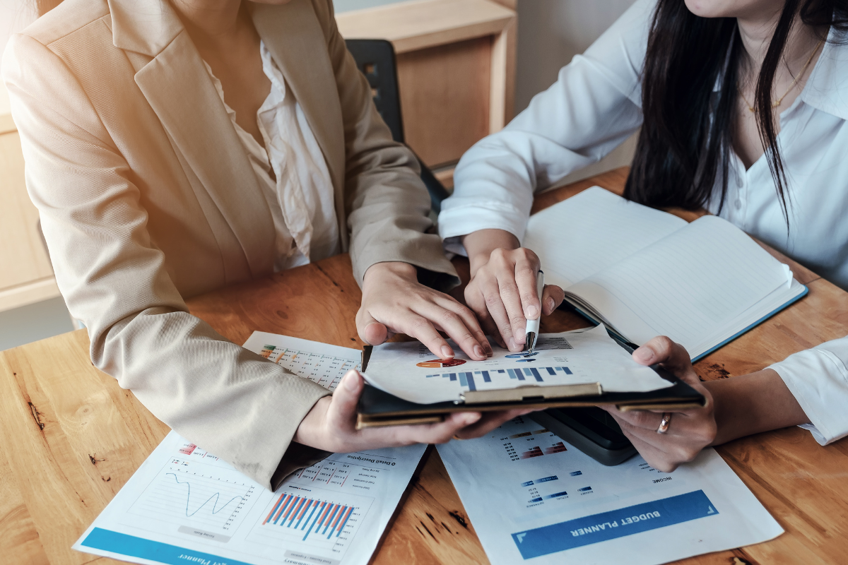 Two people pointing at a clipboard with charts